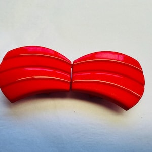 Könnte beinhalten: Zwei rote Plastik-Haarklammern mit einer gebogenen Form und drei horizontalen Rippen.