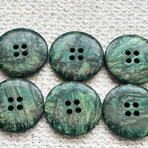 May include: Six large, round buttons with a marbled green and black pattern. Each button has four holes for sewing. The buttons are arranged in two rows of three on a textured white surface.