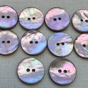 May include: Ten round buttons made of iridescent shell material, each featuring two central holes. The buttons display a shimmering surface with swirling hues of purple, blue, and pink, reflecting light with a pearlescent, multi-colored finish.