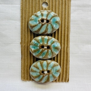 May include: Three ceramic buttons with a turquoise and brown swirl design. The oval-shaped buttons have two holes for sewing. They are attached to a brown corrugated cardboard backing.