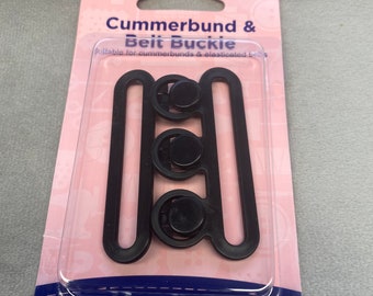 May include: A black plastic cummerbund and belt buckle set, packaged on a pink and blue card with the text "Cummerbund & Belt Buckle" and "Hemline".
