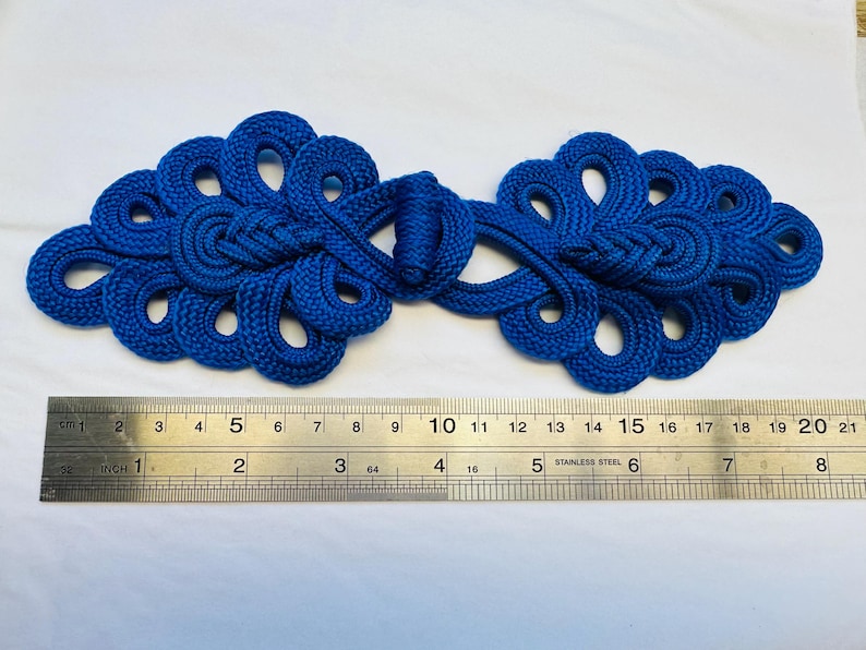 Op de afbeelding: Een paar blauwe Chinese knoop-sluitingen, ook wel bekend als knopen of sluitingen, met een decoratief ontwerp. De sluitingen zijn ongeveer 15 cm lang.
