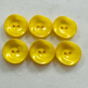 May include: Six bright yellow plastic buttons with two holes each. The buttons are round and have a slightly raised center.