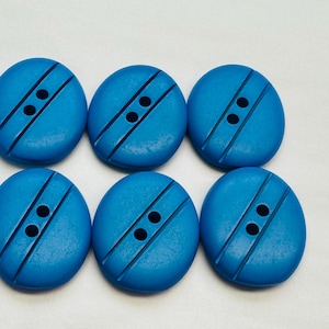 Può includere: Sei bottoni di plastica blu con due fori ciascuno. I bottoni hanno una linea rialzata al centro.