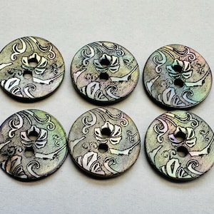 Puede incluir: Seis botones redondos con un diseño floral y de remolino. Los botones tienen un acabado nacarado con tonos verdes, azules y morados. Cada botón tiene dos agujeros para coser.