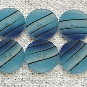 May include: Six round, translucent blue buttons with a gradient effect. Each button has two holes and is decorated with black diagonal stripes. The buttons are arranged on a white, textured surface.