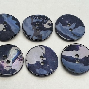 Può includere: Sei bottoni a due fori di colore blu iridescente. I bottoni hanno una superficie leggermente rialzata e arrotondata e una finitura liscia e lucida.