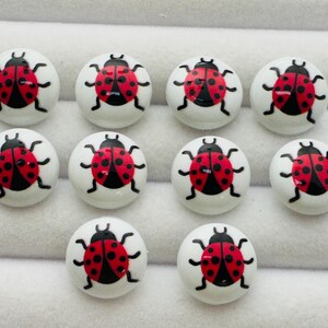 May include: Ten round white buttons, each featuring a red ladybird graphic with black spots and black legs. The buttons are arranged in three rows, with four buttons in the top row, four in the middle row, and two in the bottom row.