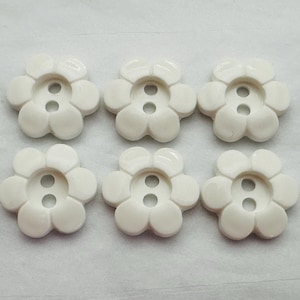 May include: Six white plastic flower-shaped buttons with two holes each.