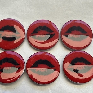 May include: Six red round coasters with a black and white image of lips printed on them.