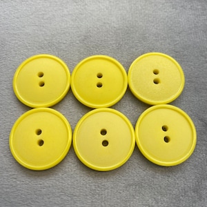 以下が含まれることがあります： 2つの穴がそれぞれ開いた黄色のプラスチックボタンが6つ。ボタンは2列3つずつに並んでいます。