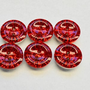 May include: Six red glass buttons with a textured surface. The buttons have two holes each.