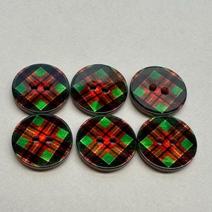 以下が含まれることがあります： 赤、緑、黒のチェック柄の丸いボタンが6つ。各ボタンには縫い付け用の穴が2つあります。ボタンは、明るい灰色の表面に3つずつ2列に配置されています。