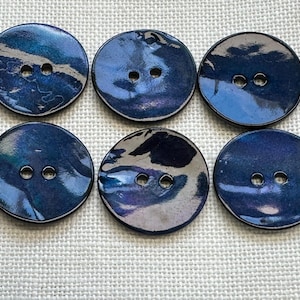 May include: A set of six round buttons featuring a glossy, iridescent finish with deep blue, purple, and black swirling patterns. Each button has two centred holes for attachment, showcasing a smooth, reflective surface with varied colour depth.