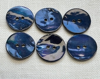 May include: A set of six round buttons featuring a glossy, iridescent finish with deep blue, purple, and black swirling patterns. Each button has two centered holes for attachment, showcasing a smooth, reflective surface with varied color depth.