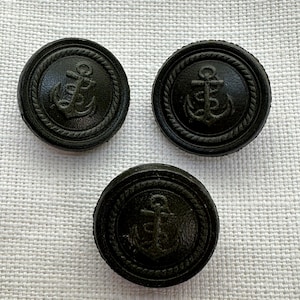 May include: Three black buttons with an anchor design. Each button features a raised anchor emblem within a rope-like border. The buttons are round and appear to be made of a solid, dark material.