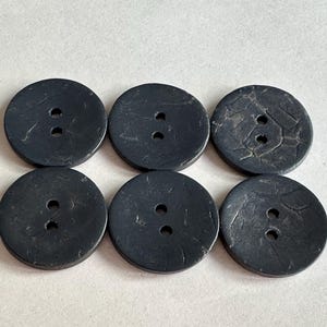 May include: Six dark grey, round buttons with two holes each. The buttons have a textured surface and are arranged in two rows of three.