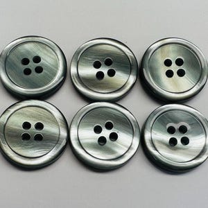 以下が含まれることがあります： 4つの穴が空いた丸い黒と灰色のボタンが6つ。ボタンは、まだら模様で、大理石のような外観です。