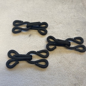 Könnte beinhalten: Drei schwarze Stoffhaken- und Klettverschlüsse. Die Verschlüsse sind für die Verwendung an Kleidung oder anderen Stoffen bestimmt.