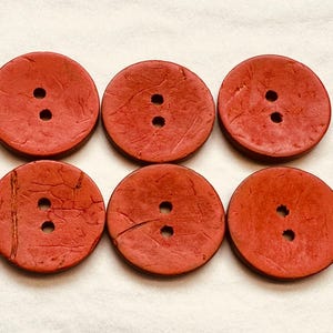 May include: Six red round buttons with two holes each. The buttons have a textured surface.
