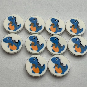 May include: Ten round wooden buttons, each with a cartoon dinosaur illustration. The dinosaurs are blue and orange on a white background. The buttons are approximately 2.5 cm in diameter.