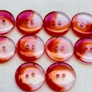 May include: A set of ten round, two-hole buttons featuring a translucent, glossy finish with swirling patterns of vibrant red and orange hues. Each button has a smooth, slightly domed surface and a clear, polished appearance throughout the set.