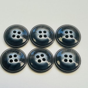 Puede incluir: Seis botones redondos de color gris oscuro, cada uno con cuatro agujeros, dispuestos en dos filas de tres. Los botones tienen un acabado brillante y un sutil efecto veteado, para costura o decoración de prendas.