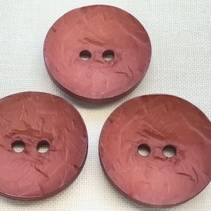 May include: Three round, dark red buttons arranged in a triangular formation. Each button features a smooth, slightly textured surface with a subtle marbled pattern and two centred holes for attachment, providing a consistent look for garments.