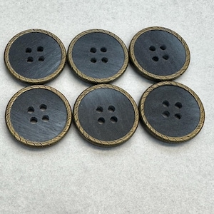 Peut inclure: Six boutons noirs avec un bord doré et quatre trous chacun. Les boutons sont disposés en deux rangées de trois.