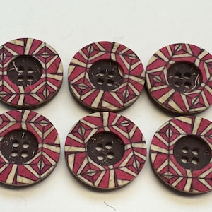 May include: Six circular buttons with a geometric pattern. The buttons have a dark brown centre with four holes and a decorative outer ring. The ring features a pattern of red and white shapes. Suitable for sewing and craft projects.