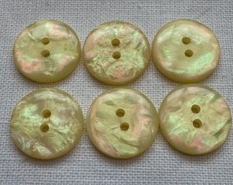 May include: Six round, iridescent buttons with two holes each. The buttons have a pearlescent finish with hints of pink and green, set against a neutral background. These buttons are ideal for sewing and craft projects.