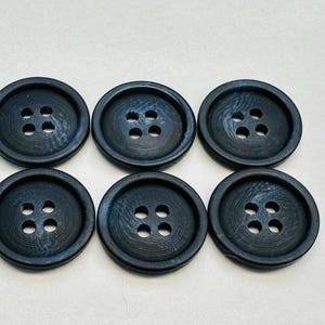 May include: Six dark blue plastic buttons with four holes each. The buttons have a slightly textured surface.