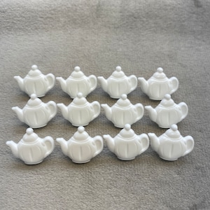 Puede incluir: Un conjunto de 12 botones blancos en forma de tetera. Los botones son de plástico y tienen un acabado liso y brillante.