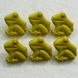 May include: Six green frog buttons with black eyes and a yellow belly. The buttons are made of plastic and have a glossy finish.