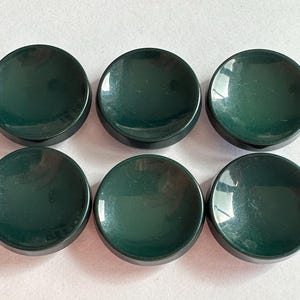 May include: Six dark green, round, small dishes are arranged in two rows of three. The dishes have a slightly concave center and a raised, rounded edge. The glossy finish reflects light, highlighting their smooth surface.