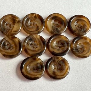 May include: Ten round buttons with a marbled appearance in shades of brown and tan. Each button has four holes and a slightly raised center. The buttons are arranged in a grid pattern.