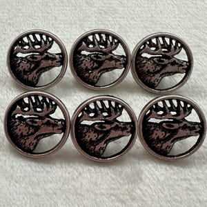 May include: Six silver-coloured buttons with an elk head design. Each button has a circular frame around the elk's profile, showing its antlers and facial features. The buttons are arranged in two rows of three.