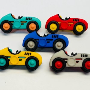May include: A selection of toy race cars in teal, red, blue, yellow, and grey. Each car has a black interior, black tyres, and contrasting coloured wheels. The cars are designed with a classic, vintage aesthetic.
