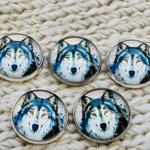 May include: Five circular buttons featuring a detailed illustration of a wolf face with blue, black, and white fur tones. Each button has a smooth, glossy, domed surface and a polished silver-toned metal rim, arranged in a group of five individual pieces.