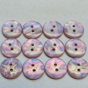 May include: Twelve iridescent, round buttons, each with two holes. The buttons display a swirling pattern of pink, purple, and blue. These decorative buttons are suitable for sewing and craft projects.