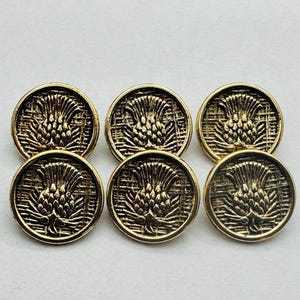 以下が含まれることがあります： アザミのデザインが施された、金色のボタンが6つ。ボタンは丸く、わずかに浮き出たレリーフ模様があります。アザミが中心的なデザイン要素で、複雑なディテールが特徴です。