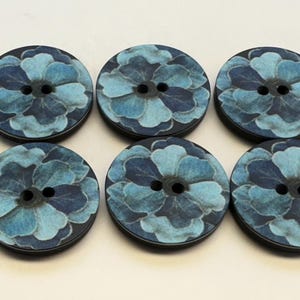 May include: Six round buttons with a floral design. The buttons feature a dark blue rim and a light blue and dark blue floral pattern. Each button has two holes for sewing.