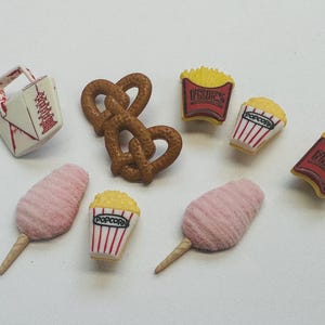 May include: A selection of miniature food items including a Chinese takeaway box, pretzels, popcorn, candy floss, and chips. The popcorn and chips are in red and white striped containers. The candy floss is pink.