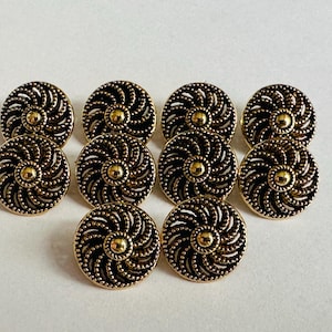 Può includere: Una collezione di dieci bottoni decorativi. Ogni bottone presenta un centro dorato e un design a filigrana nera a spirale attorno ai bordi. I bottoni sono rotondi e hanno un'estetica vintage.