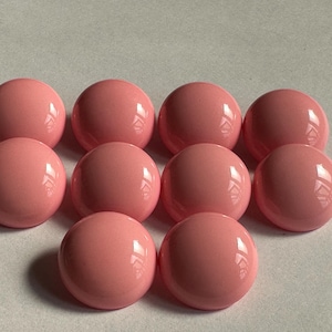 May include: A collection of ten glossy, light pink, spherical beads. The beads are arranged in a cluster, with each sphere reflecting light. The smooth, rounded shapes and consistent color create a visually appealing pattern.