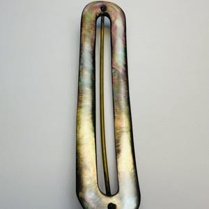Puede incluir: Una horquilla para el cabello nacarada con un diseño en forma de U. La horquilla presenta una superficie brillante e iridiscente con un pasador de metal dorado en el centro. La horquilla mide aproximadamente 10 cm de largo.