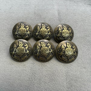 May include: Six gold-toned metal buttons with a detailed design featuring a crown and lions. The buttons are round and have a raised design.