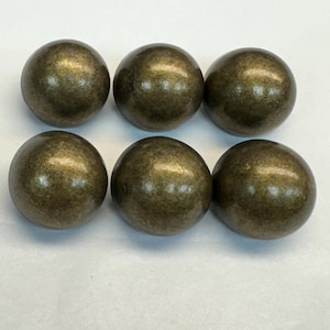 Puede incluir: Seis clavos decorativos esféricos de color bronce dispuestos en dos filas de tres. Cada cabeza de clavo tiene una superficie redondeada y lisa con un aspecto ligeramente texturizado. El color es una mezcla de oro y marrón.
