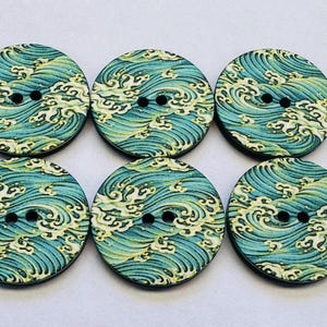May include: Six round wooden buttons with a Japanese wave pattern in shades of teal, blue, and yellow. Each button has two black sewing holes. The buttons are approximately 1.5 inches in diameter.