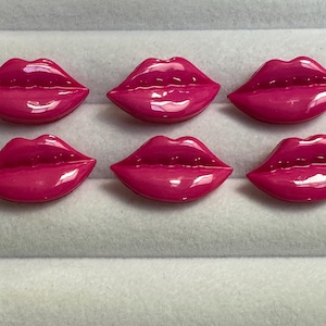 May include: Six pink plastic buttons shaped like lips. The buttons are glossy and have a 3D effect.